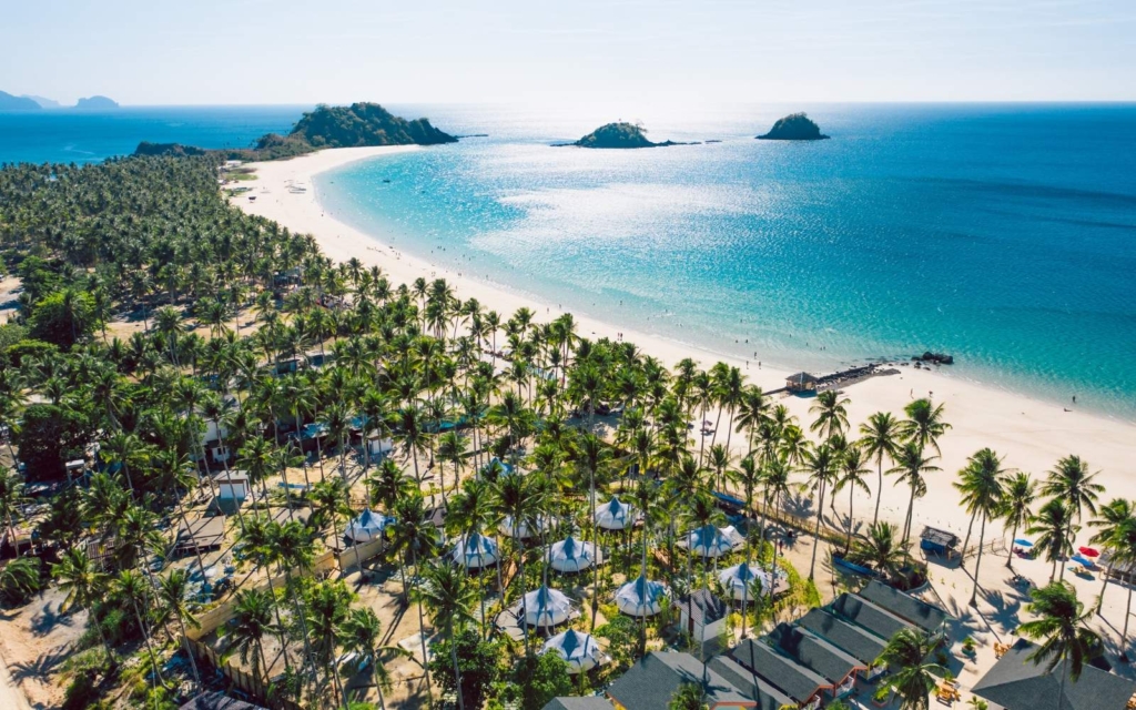 Aerial image of Nacpan Beach Resort, palm trees, blue water, and white sand