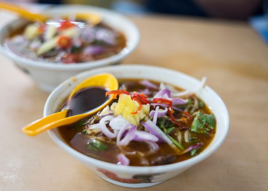 Assam Laksa Penang in white bowl with yellow spoon