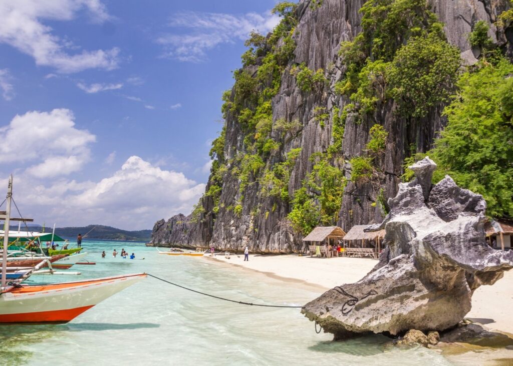 Boats on beach of Coron with large rock wall