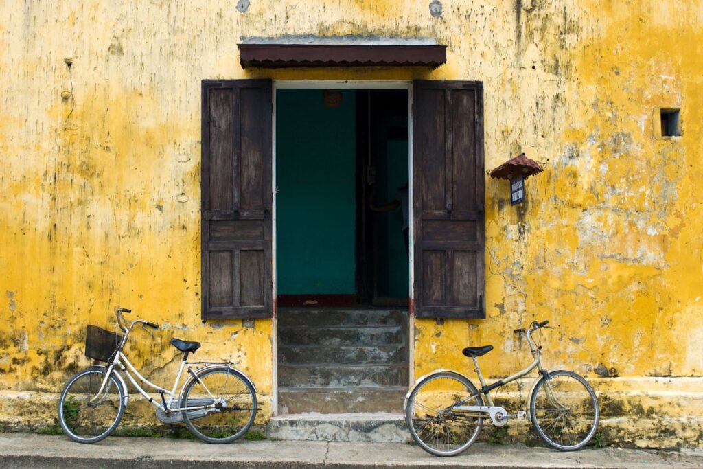 Bikes leaning against a yellow wall with brown shutters in Hoi An