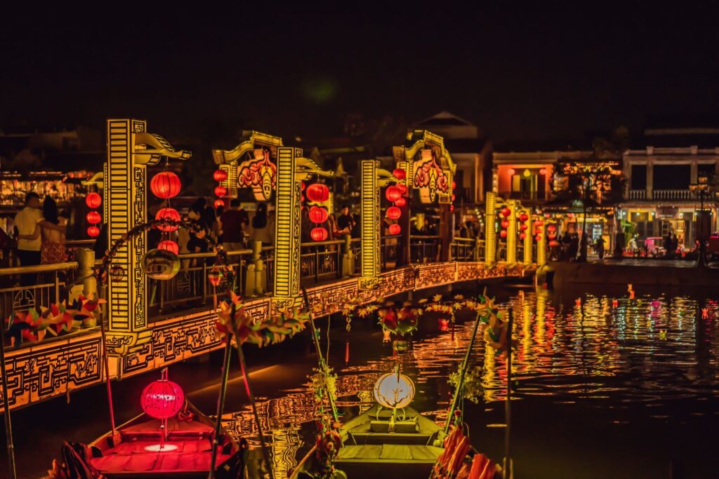 Boats on the river in Hoi An at night with lighted bridge