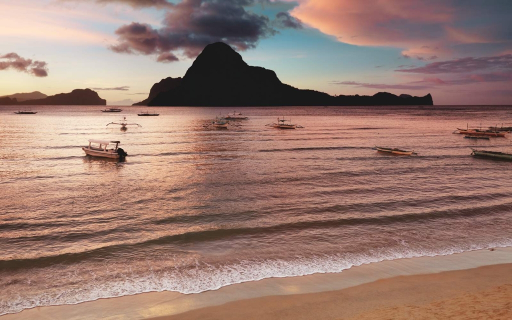 Caalan Beach at sunset with island and boats in the water, one of the best places to stay in Palawan.