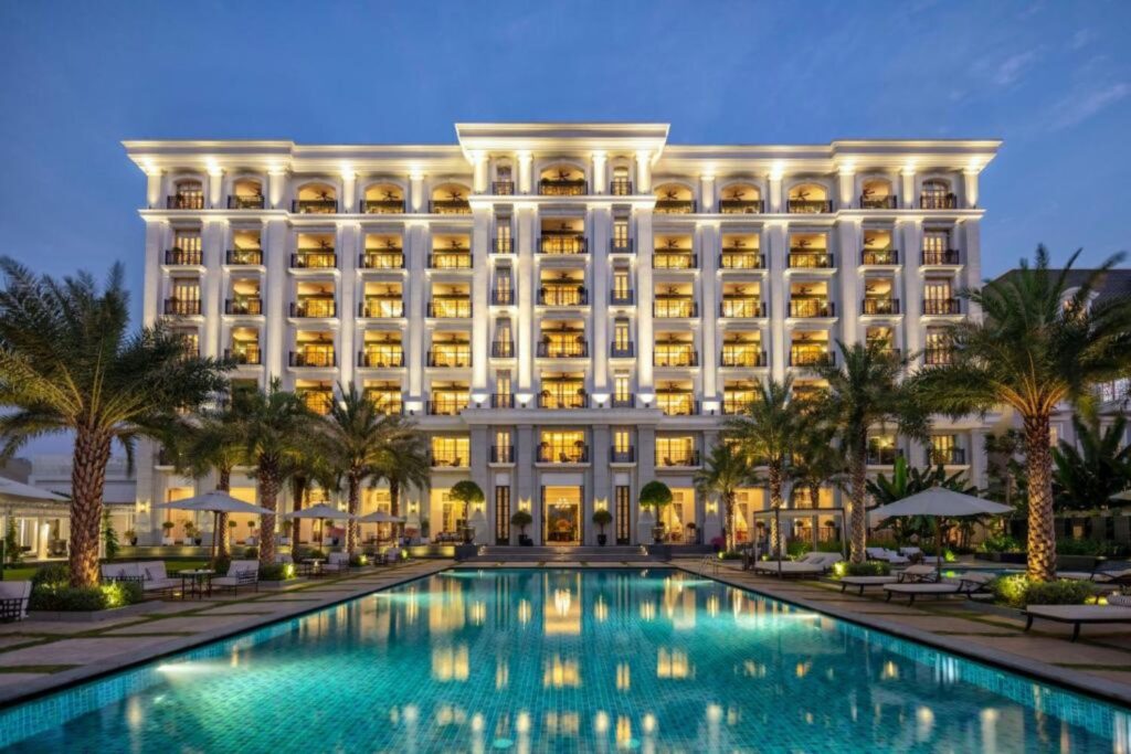 Exterior view of Mia Saigon hotel in Ho Chi Minh City with outdoor swimming pool and palm trees at night