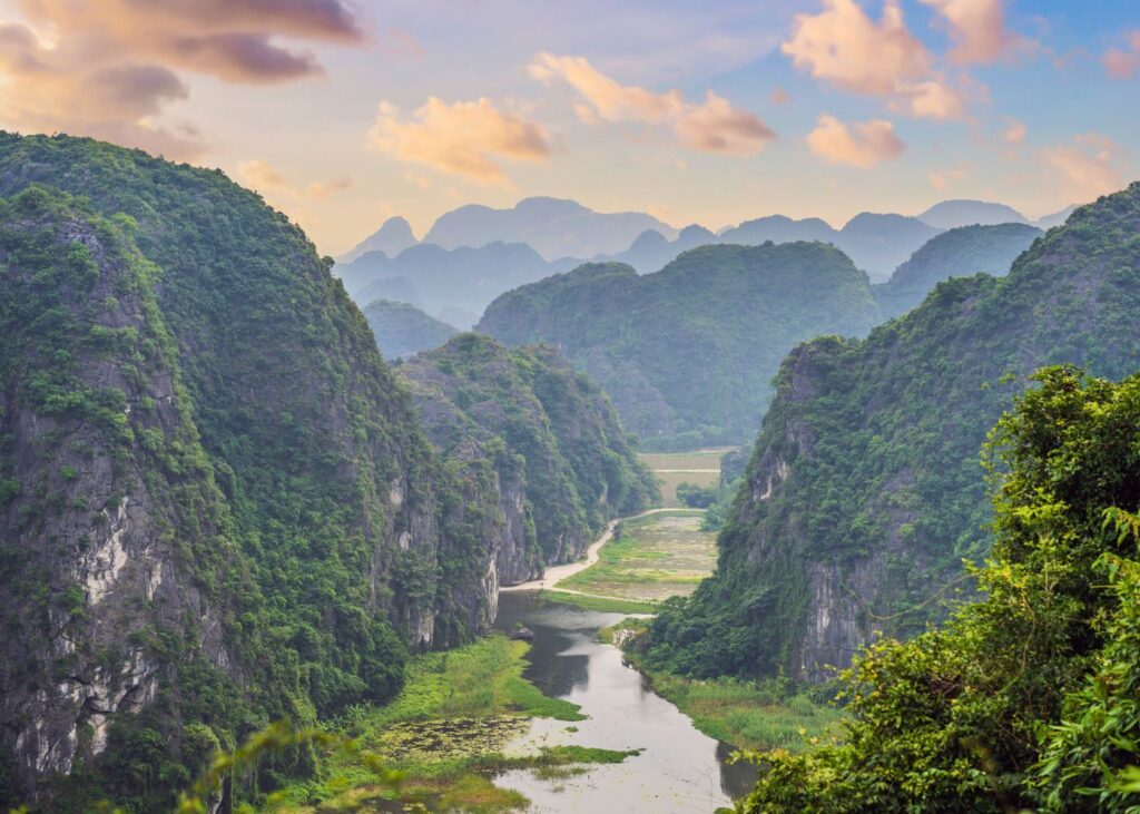 Hazy morning in Tam Coc Vietnam with river, pink clouds, and mountains