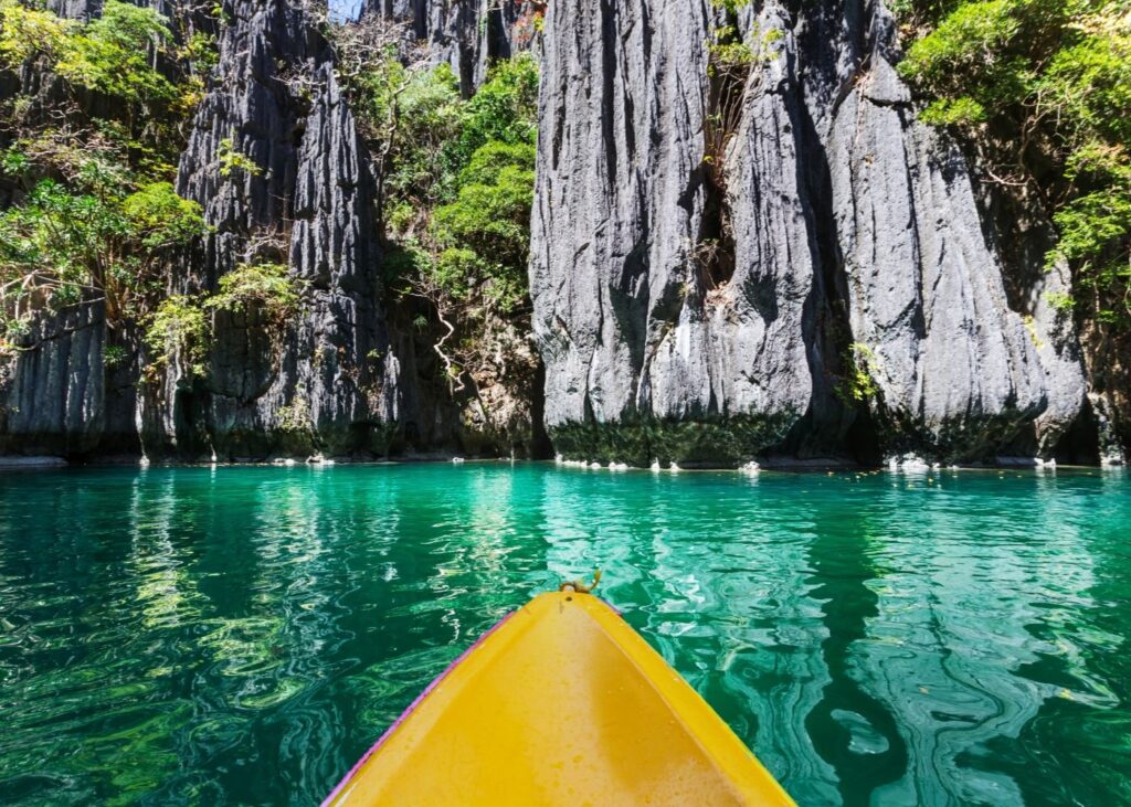 yellow kayak in green waters of El Nido Palawan with limestone karsts