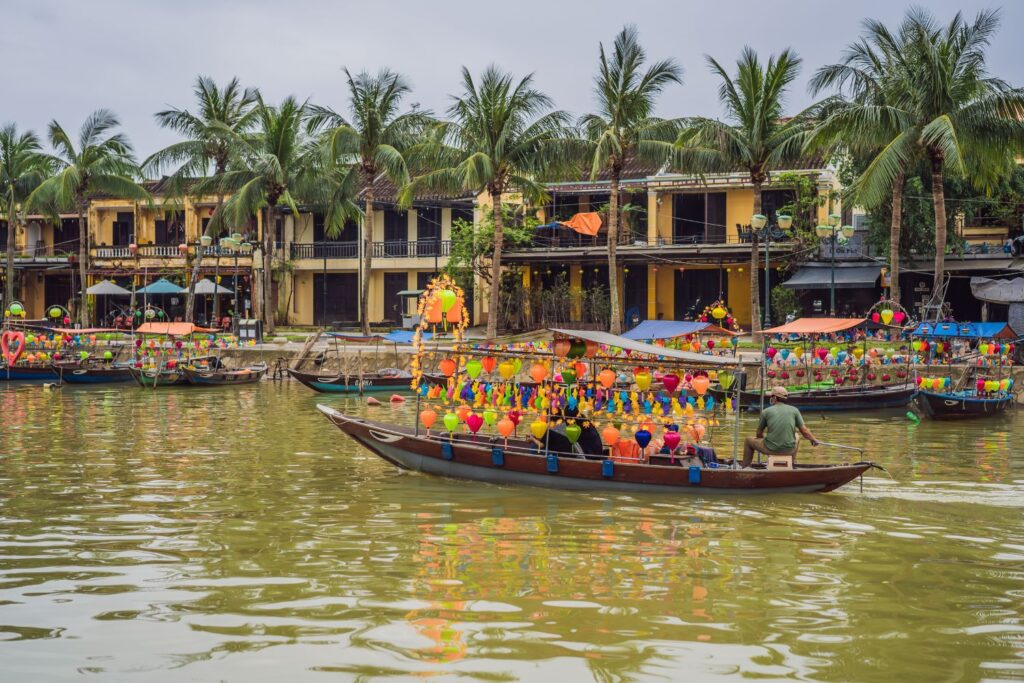 Lantern covered boats in the canal of Hoi An with yellow buildings and palm trees