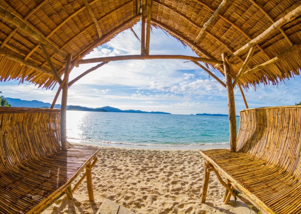 Grass hut and sand in Palawan with ocean in background