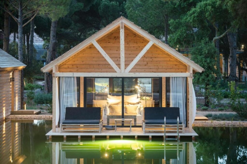 luxurious wooden house with glass windows above the water surrounded by trees