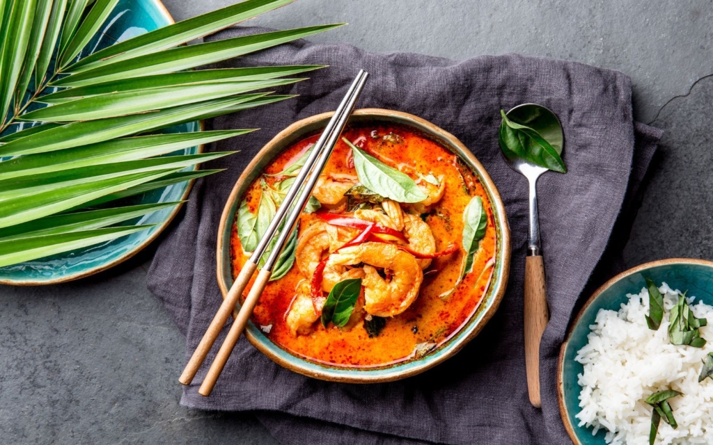 Thai traditional red curry soup with shrimp on a gray background with greenery and rice