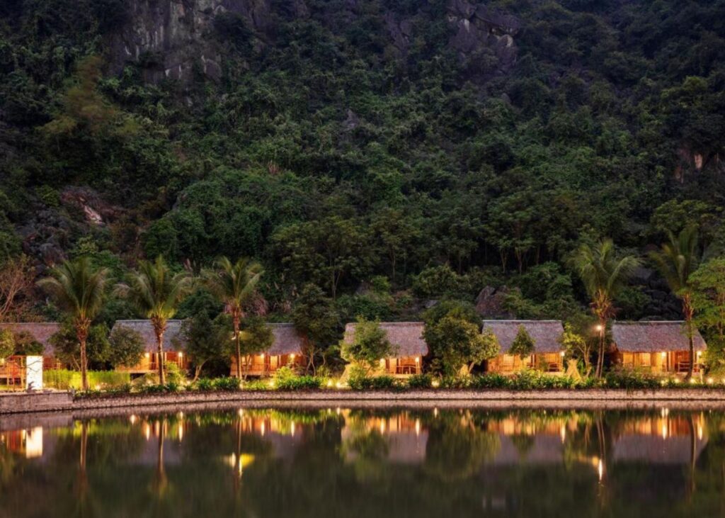 Traditional huts along a lake with forested background at An's Eco Resort