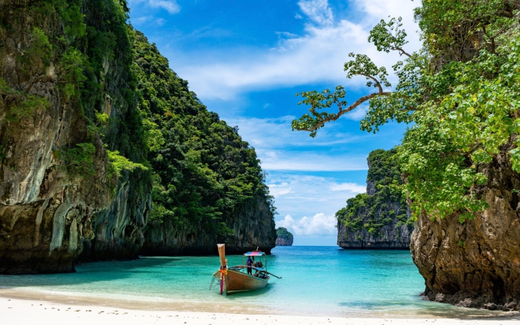 Traditional longboat in a bay with towering limestone karsts in Thailand with blue sky and clouds
