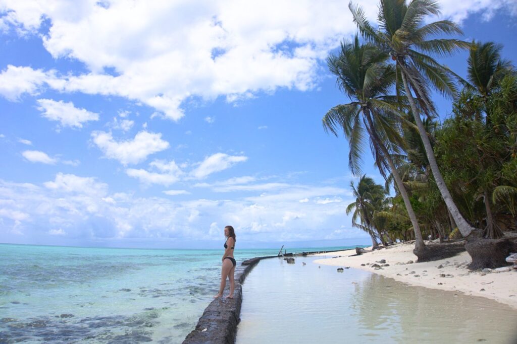 Woman walking along the beach in Balabac Palawan with shallow water, palm trees, and a blue sky with clouds