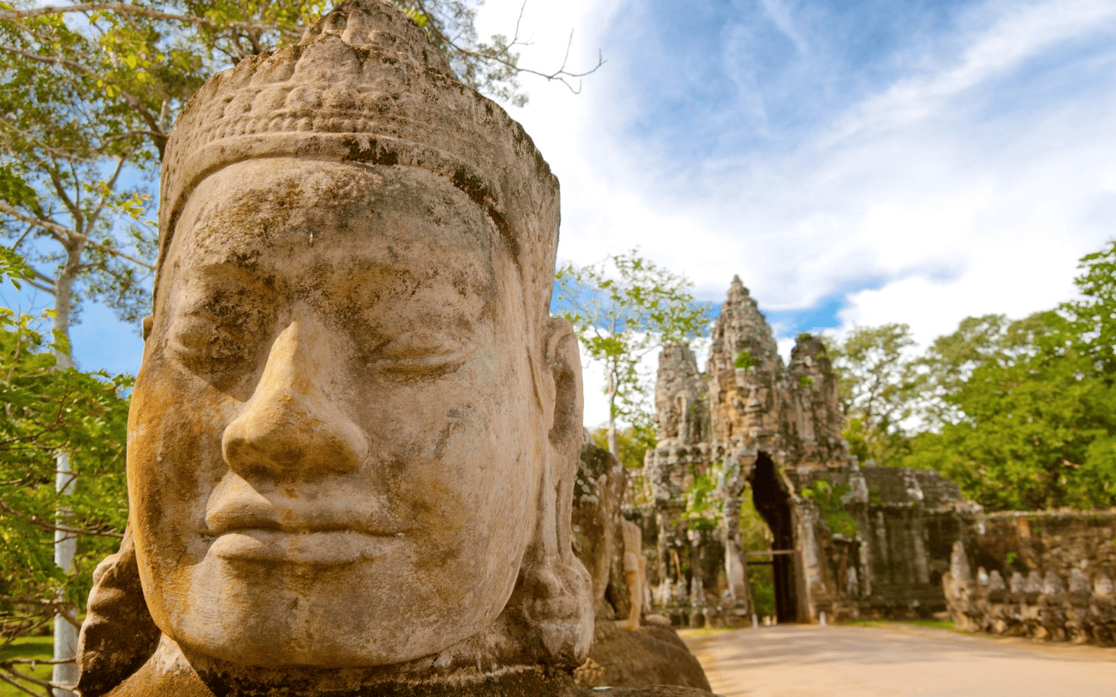 Large head statues by the gate of Angkor Wat with jungle backdrop