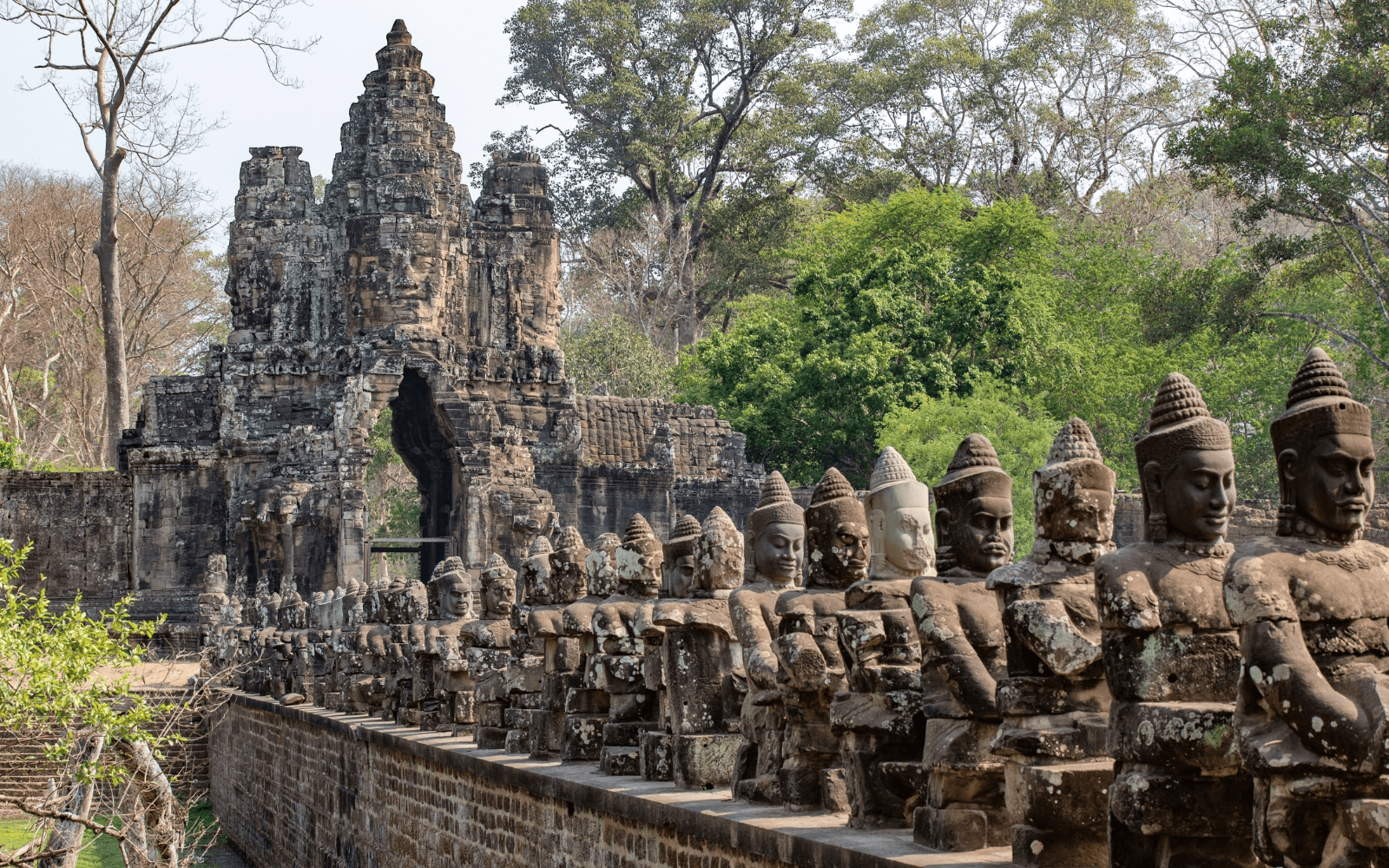 Gate and row of carved statues at Angkor surrounded by jungle