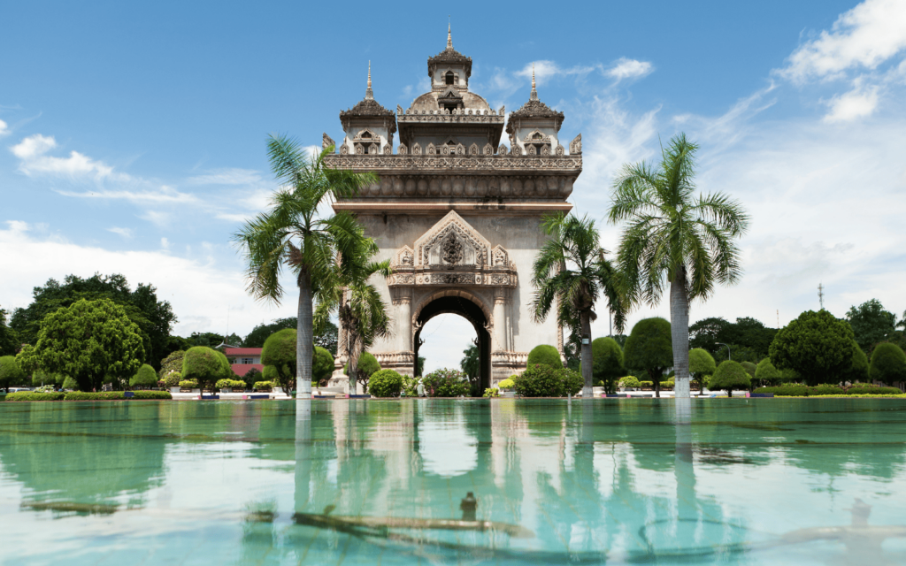 Patuxay Monument against a backdrop of greenery with a turquoise pool in front, one of the symbols of the capital city of Laos, Vientiane.