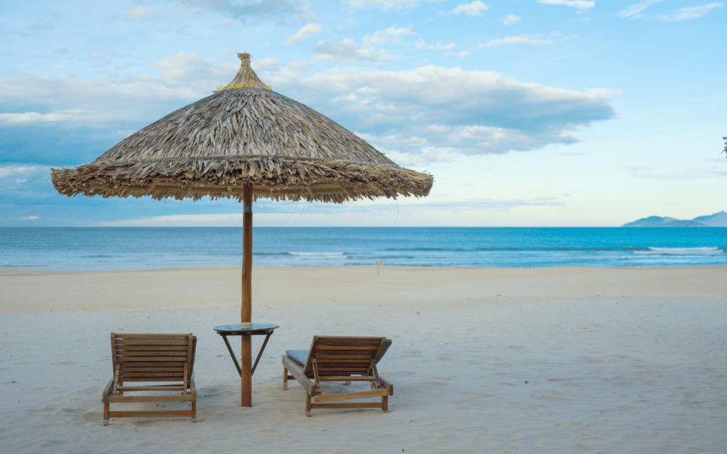 Thatch My Khe Beach umbrella and chairs on the sand with water and mountans in the background in Da Nang Vietnam