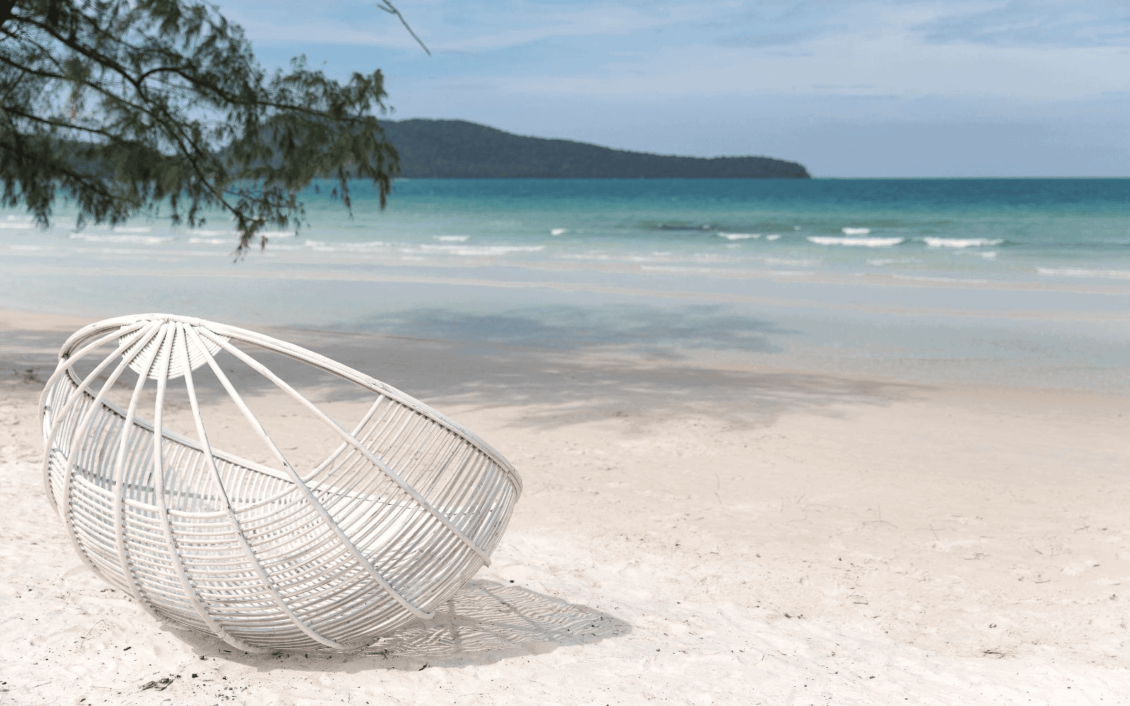 White chair on a white sand beach with bright blue waters and a mountain in the distance on Saracen Beach