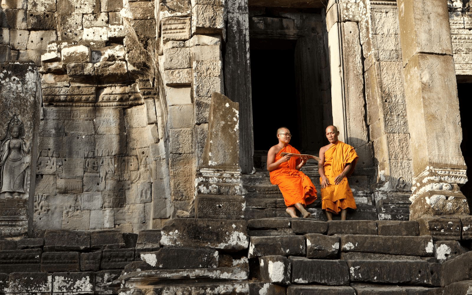 Two Buddhist monks sitting on the steps of an ancient temple in Cambodia
