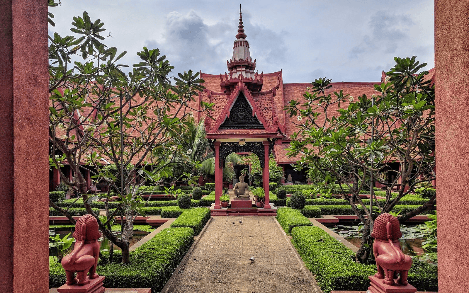 Red sandstone pagoda with Buddha statue and lions in a green garden in Phnom Penh